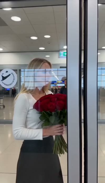 Hand-held tracking through the arrivals gate as a traveler comes into view — they lock eyes, she drops the bouquet and runs into his arms, camera circles them. Audio: airport PA, distant rolling luggage, warm orchestral swell, heartbeat rising.